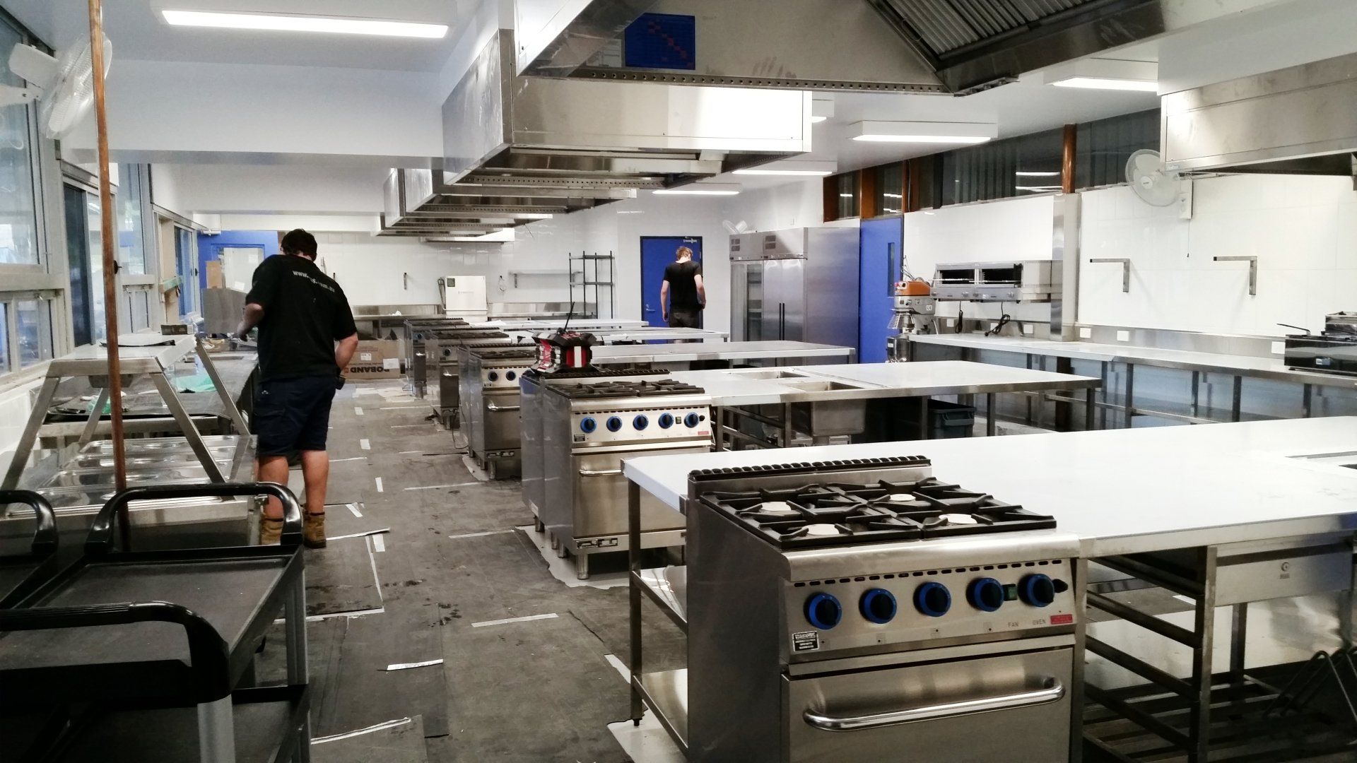 A man is standing in a large kitchen with lots of stainless steel appliances.