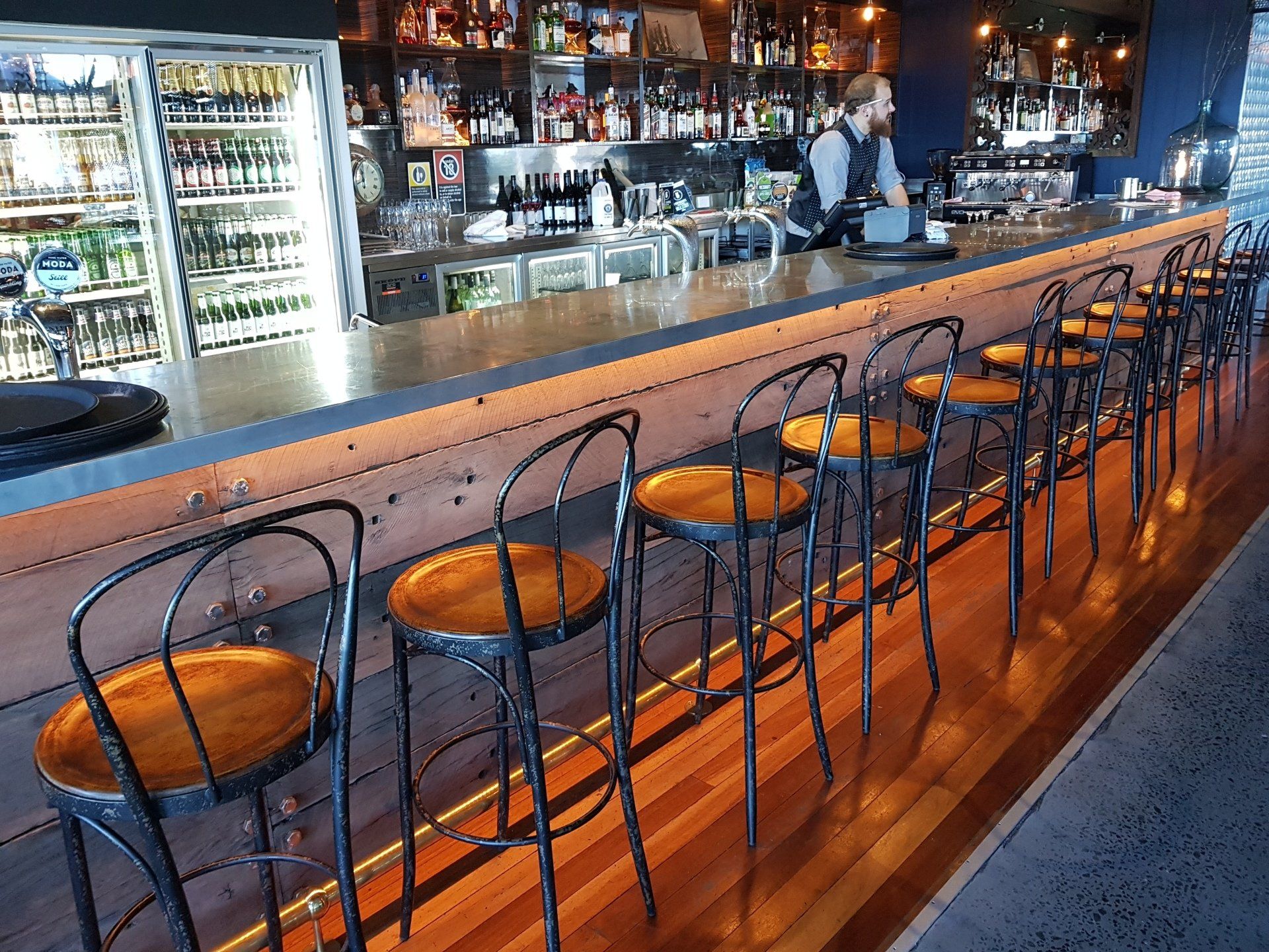 A row of bar stools are lined up along a long bar in a restaurant.
