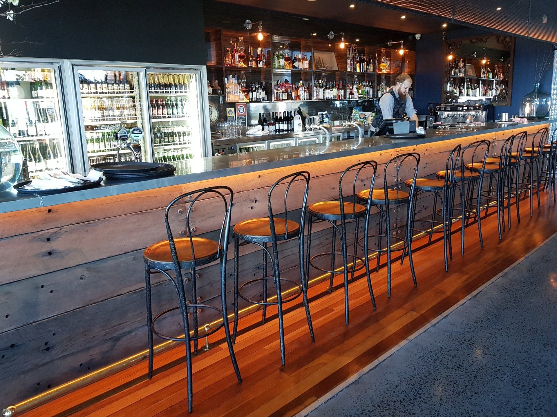 A row of bar stools are lined up along a long bar in a restaurant.