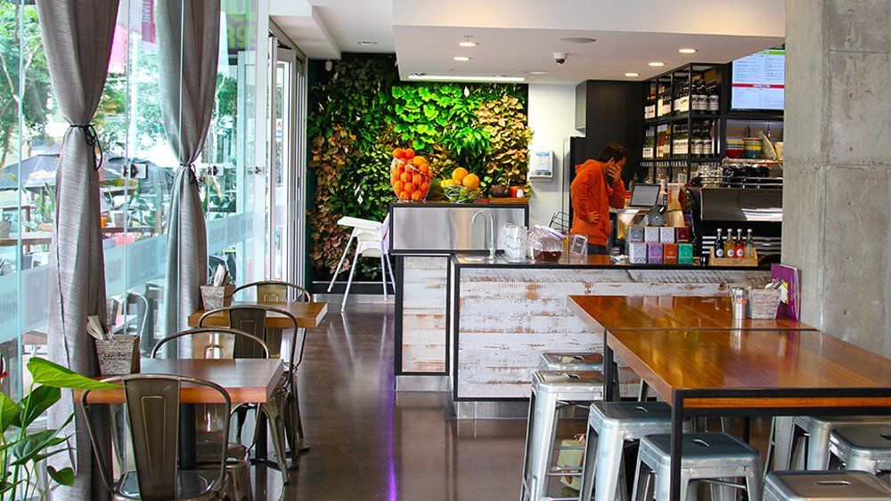 A restaurant with tables and chairs and a man standing at the counter.