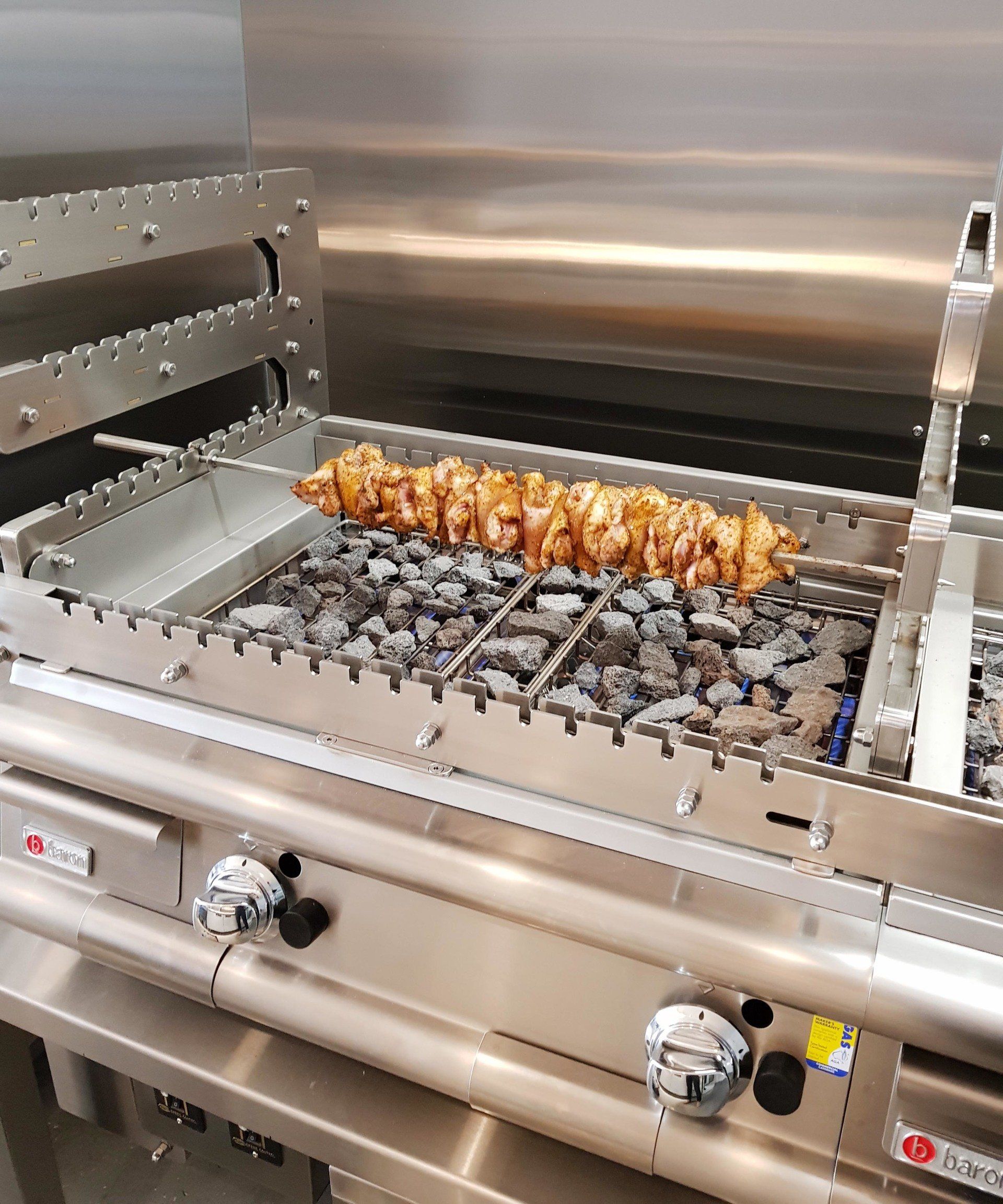 A stainless steel grill with chicken on skewers cooking on it.