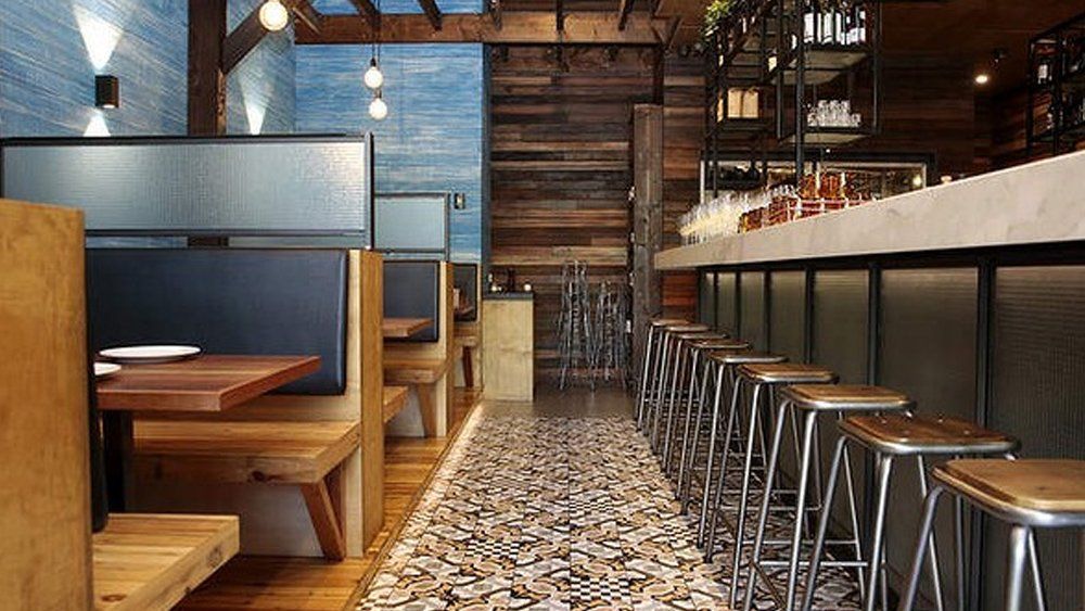 A restaurant with tables and stools and a bar.