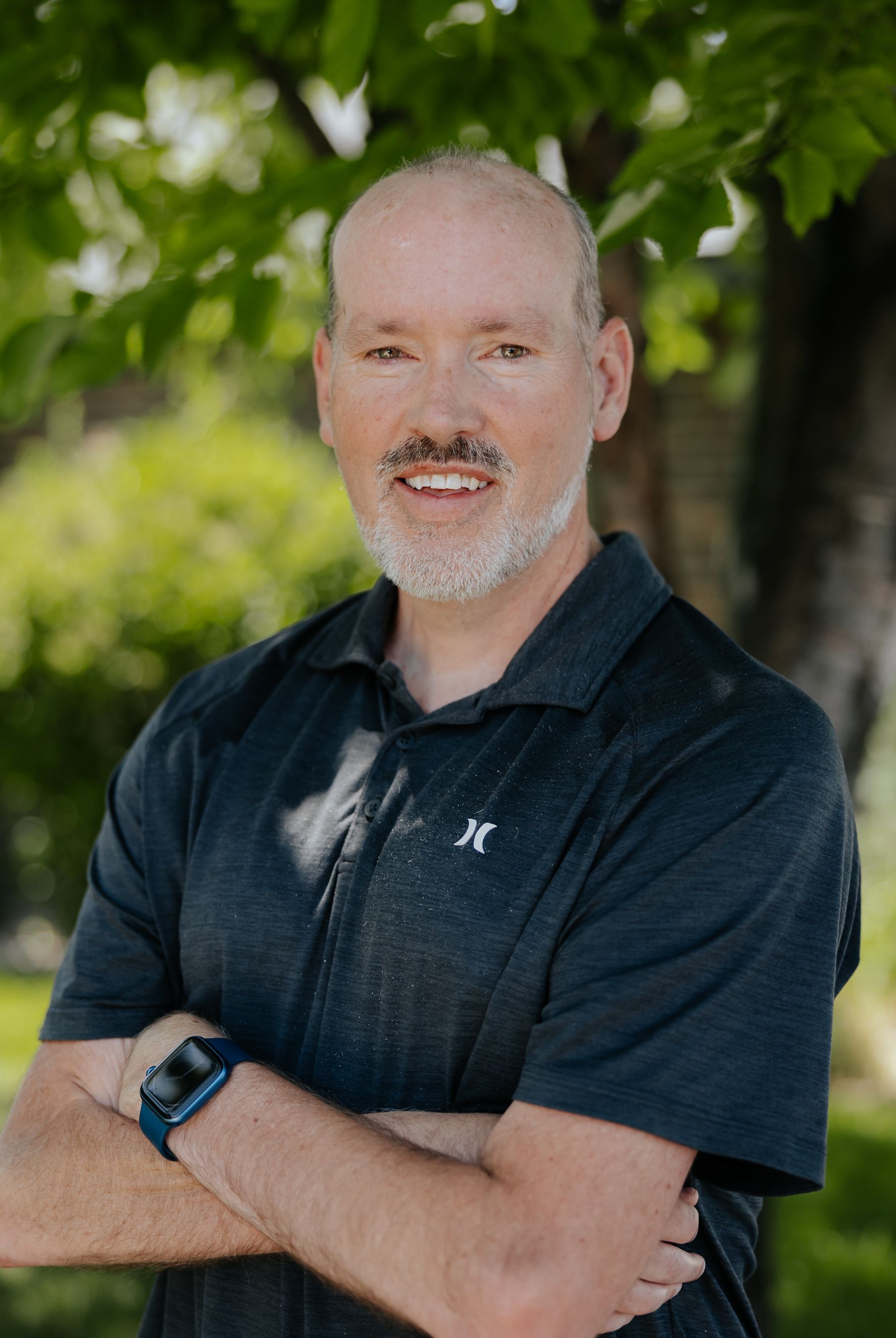 A bald man in a blue shirt is smiling for the camera.