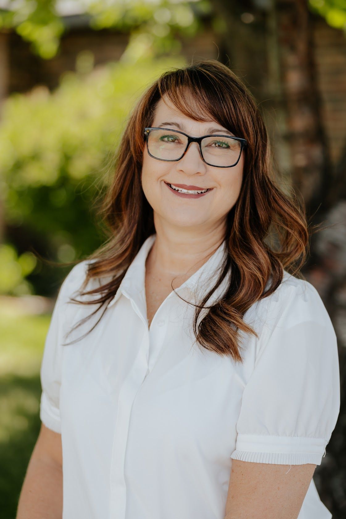 A woman wearing glasses and a blue jacket is smiling for the camera.