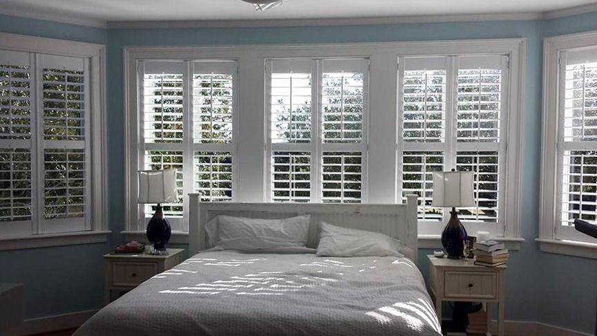 A bedroom with a bed and lots of windows with shutters
