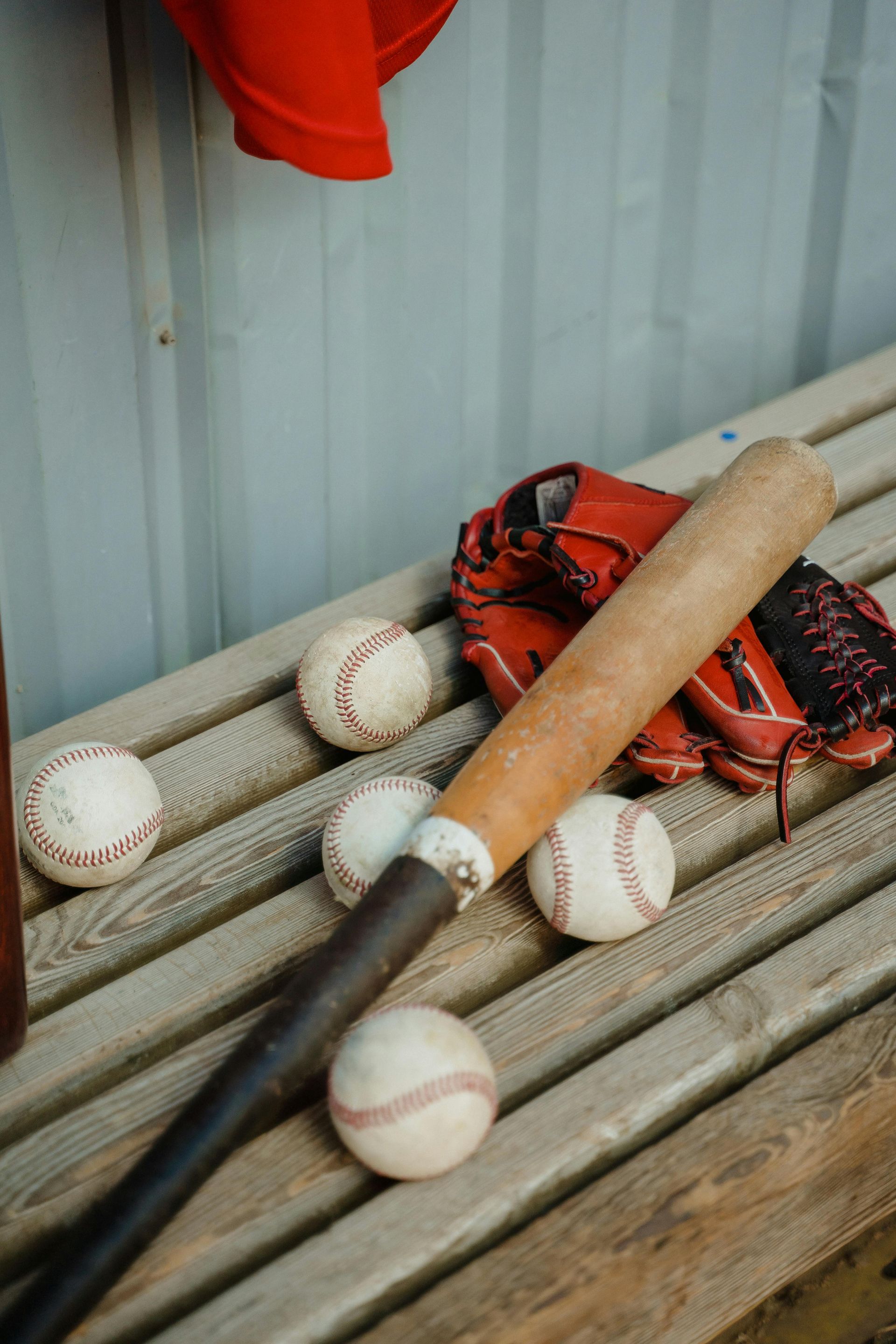 Baseball bat, glove, and several baseballs on a weathered bench