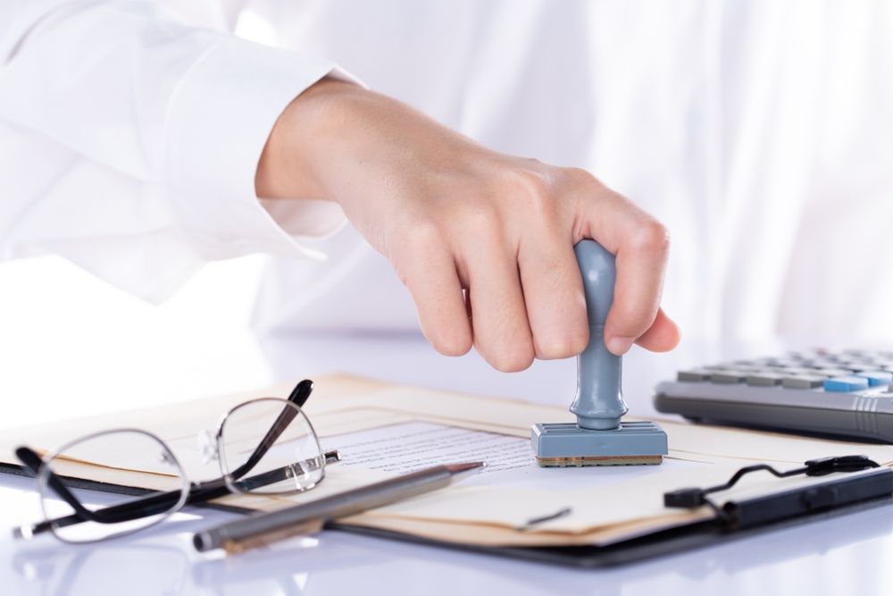 Hand stamping a document at a desk with calculator, glasses, and pen