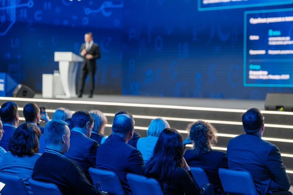 Audience watching a speaker on a blue-lit conference stage