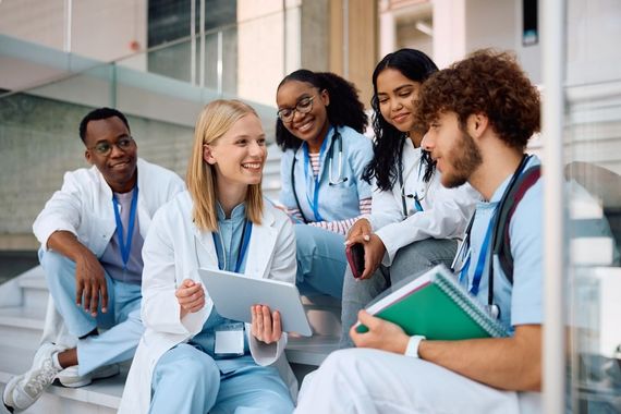 Medical students in white coats studying together on a stairway with notebooks and tablets