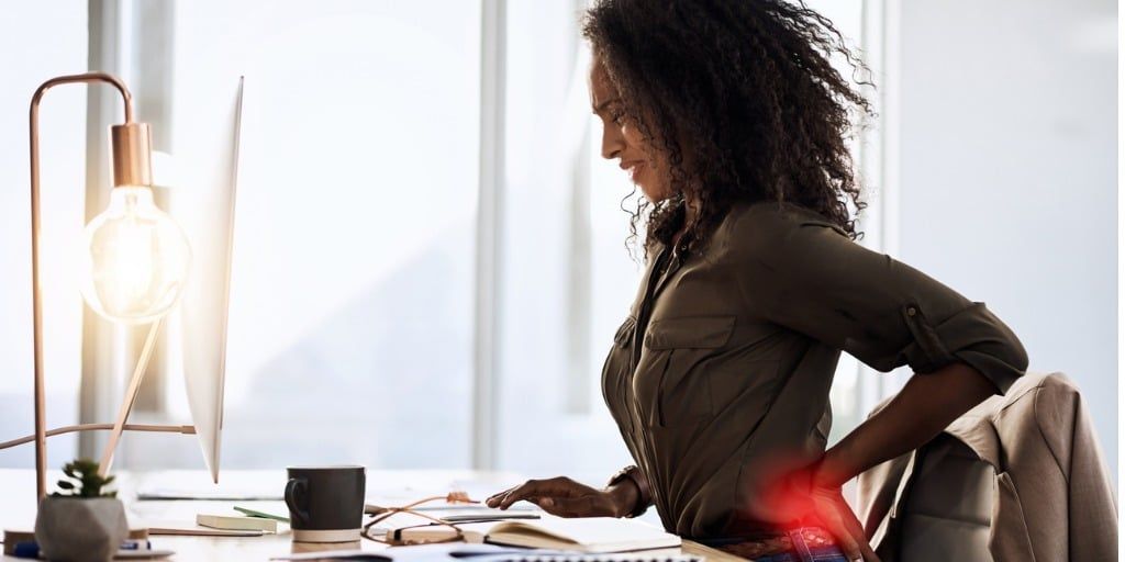 a woman is sitting at a desk with her back in pain