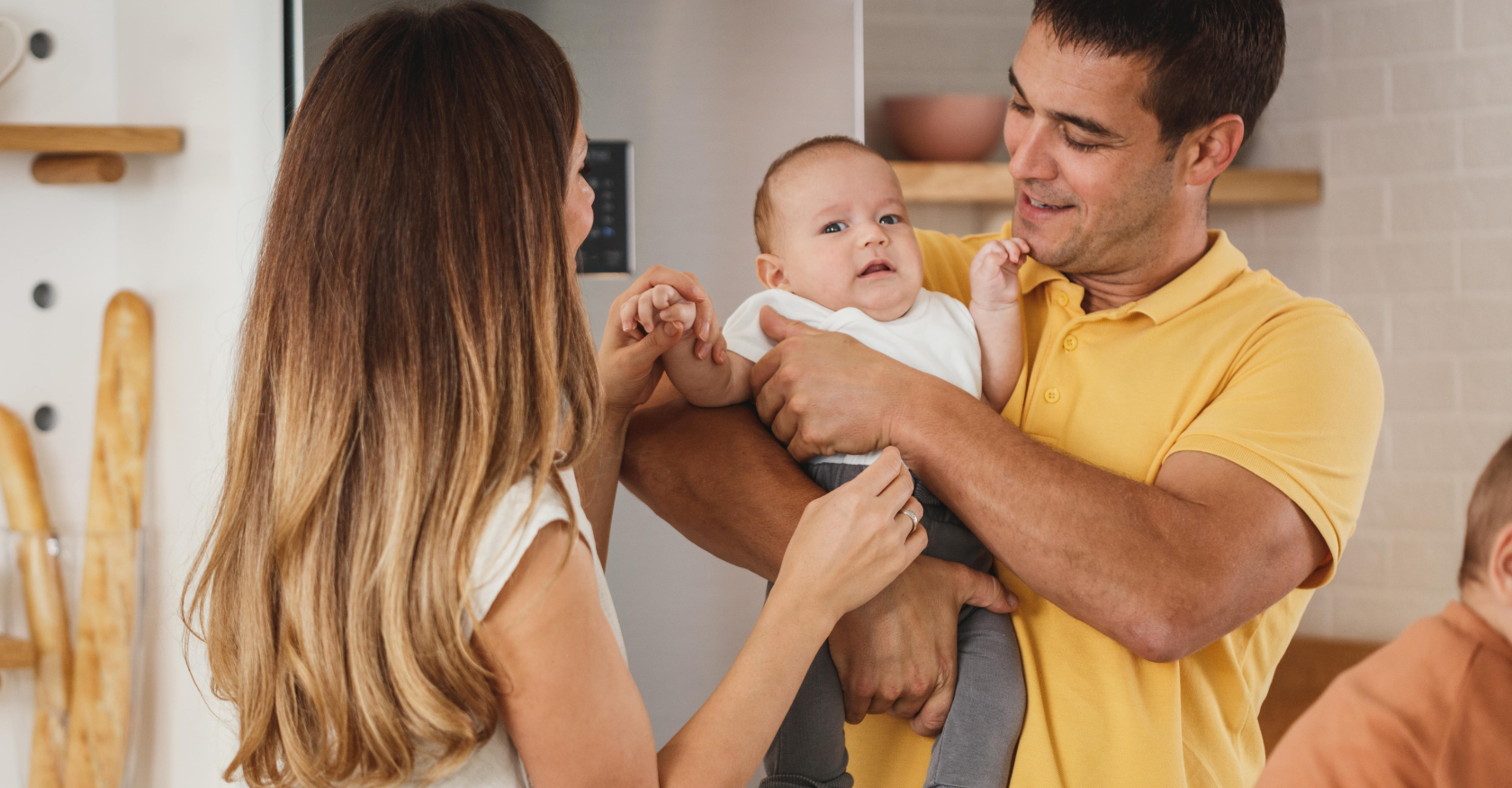 A man and woman are holding a baby in their arms in a kitchen.