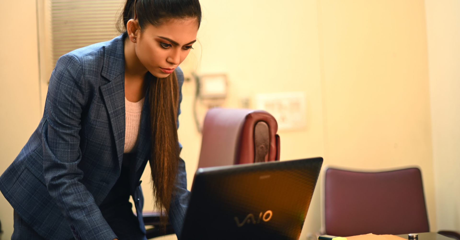 A woman in a suit is standing in front of a laptop computer.