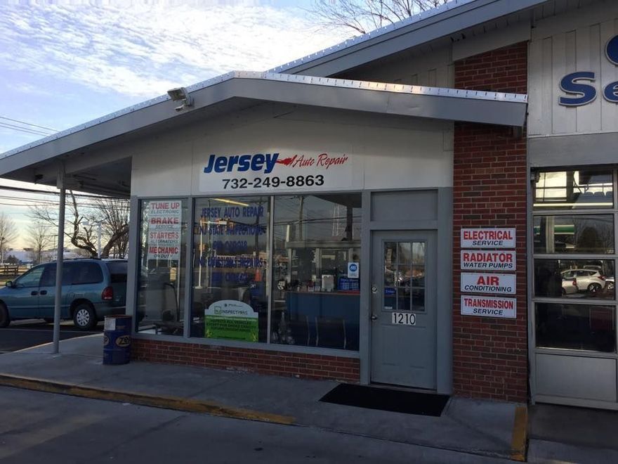 A white building housing Jersey Auto Repair, with a glass storefront, gray door, and brick pillar listing repair services.