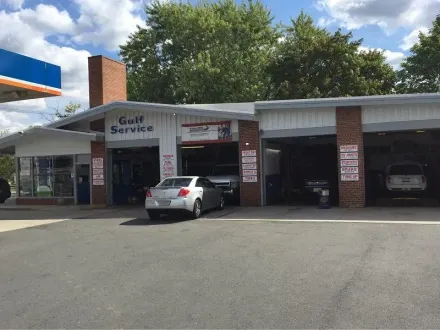 A multi-bay Gulf Service automotive repair station with a white sedan parked in front under a partly cloudy sky.