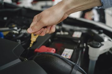 A person checking the oil level of a car engine using a yellow dipstick.