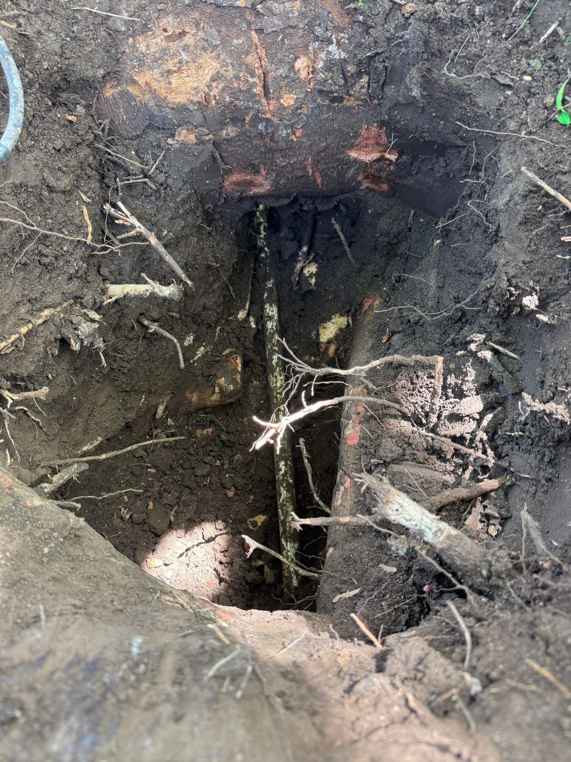 A rectangular hole in the ground with exposed copper pipes and dark soil.