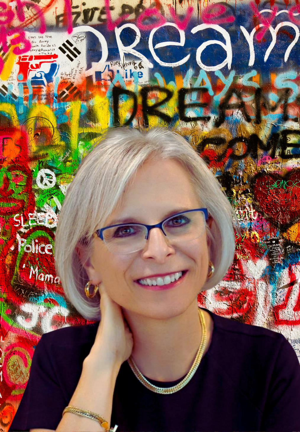 A woman wearing glasses is smiling in front of a graffiti wall.