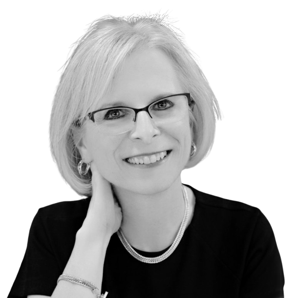 A woman wearing glasses and a necklace is smiling in a black and white photo.