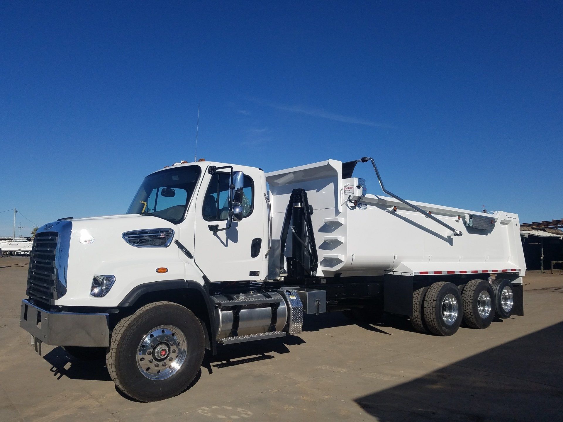 A white dump truck is parked in a dirt field.