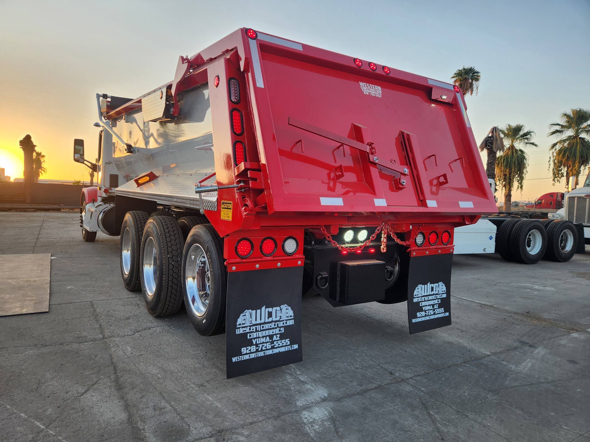A red dump truck is parked in a parking lot at sunset.