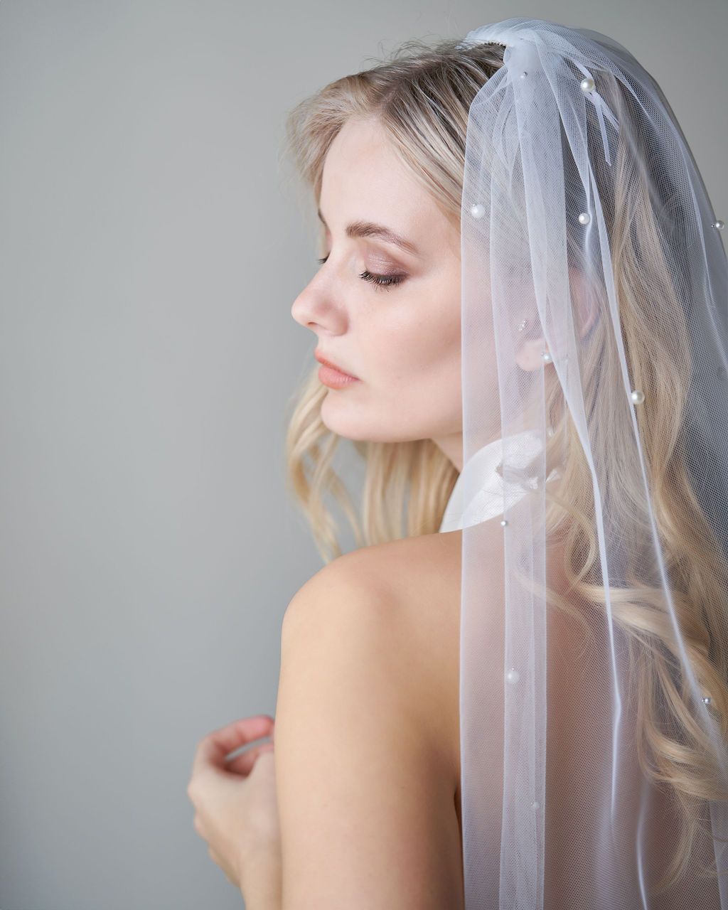 A woman is wearing a white veil with pearls on it.