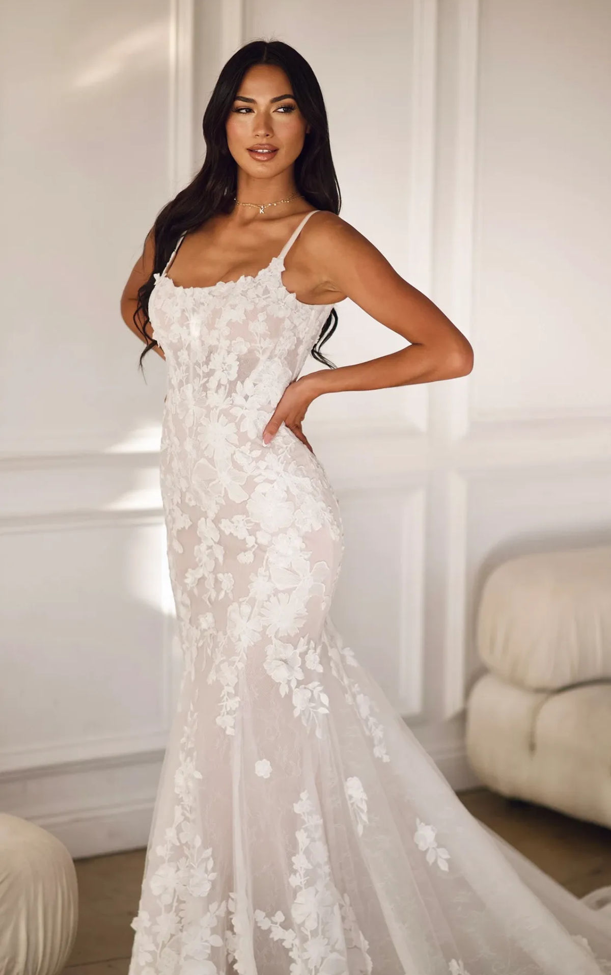 A woman in a white wedding dress is standing next to a couch.