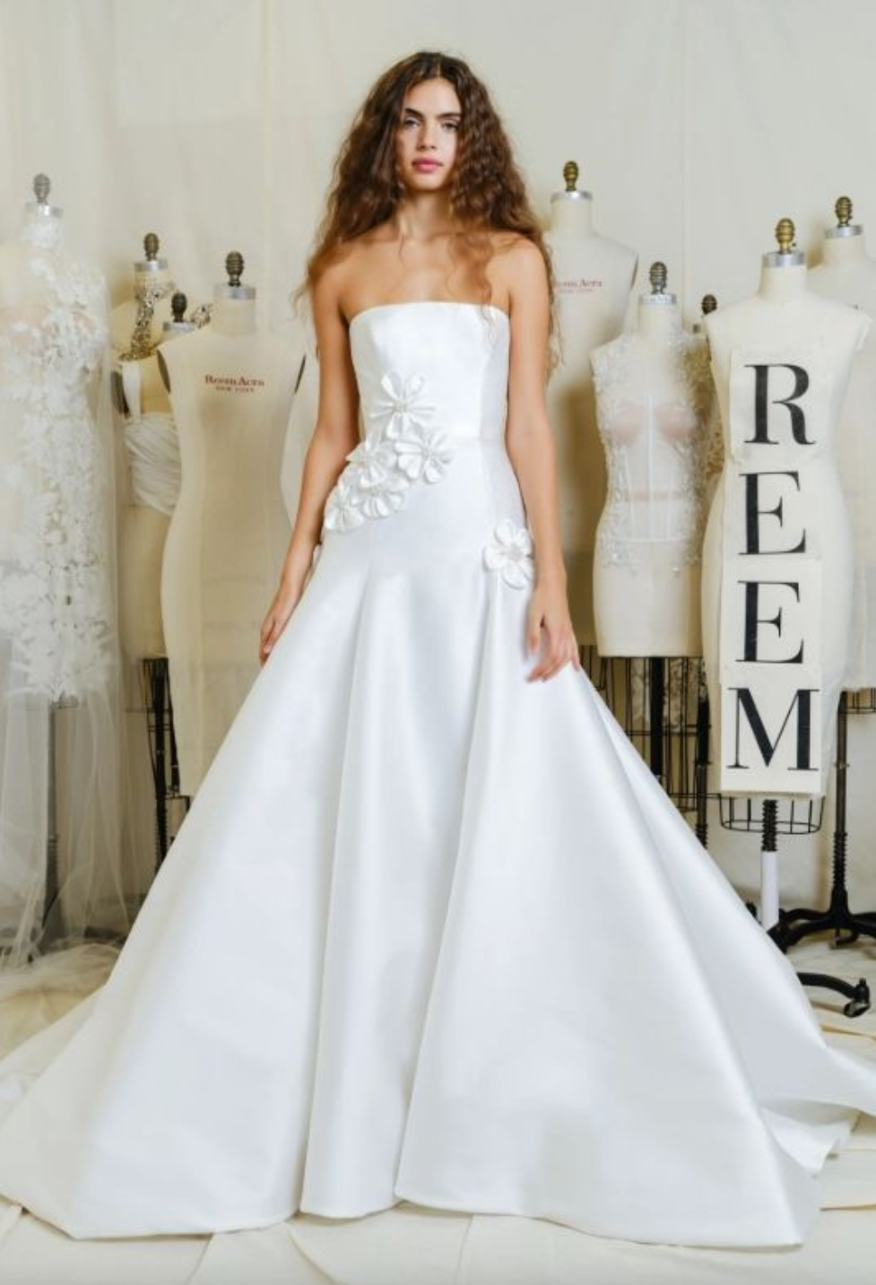 A woman in a wedding dress is standing in front of a body of water holding a bouquet of flowers.