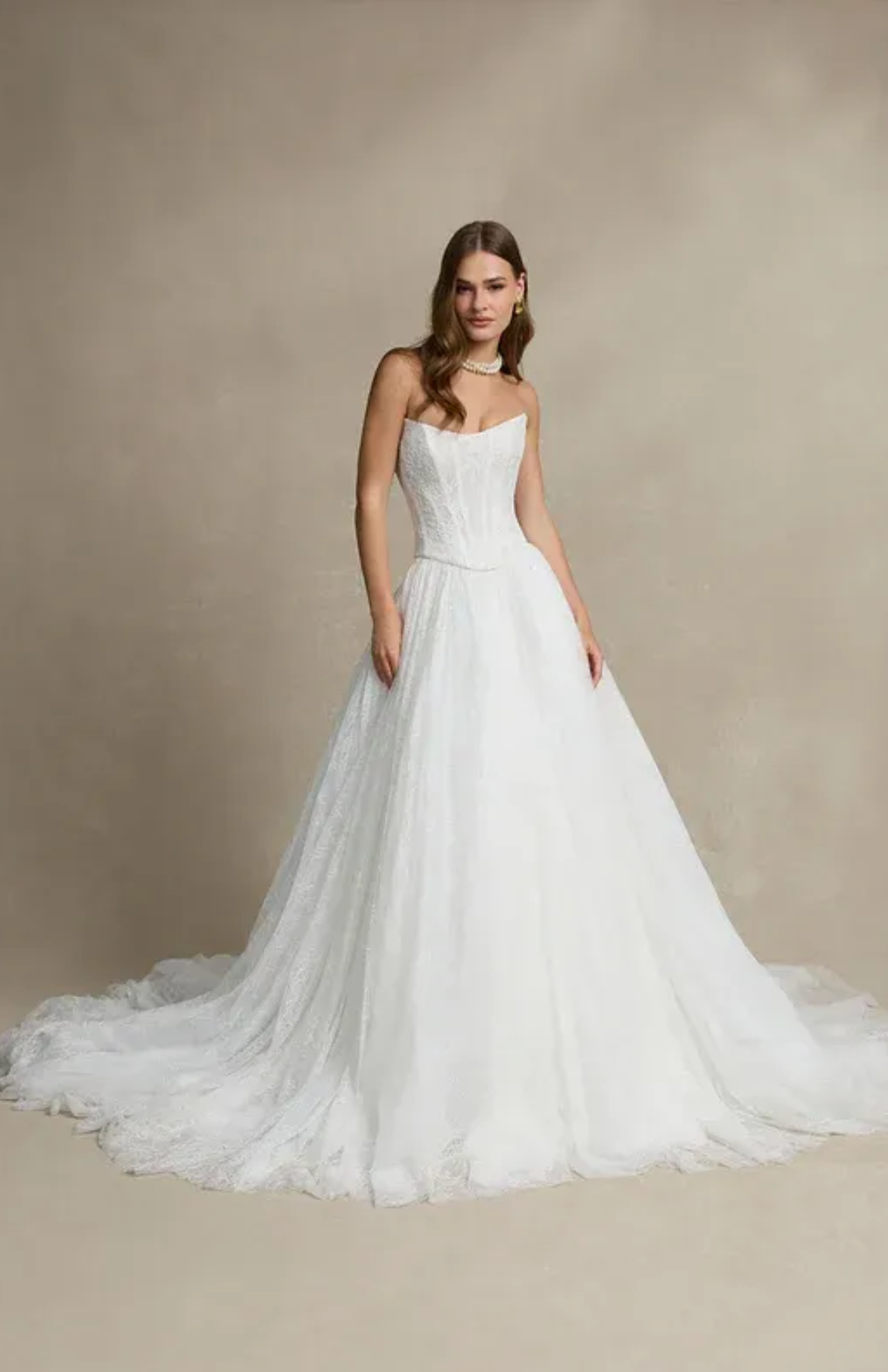 A woman in a white lace wedding dress is leaning against a brick wall.