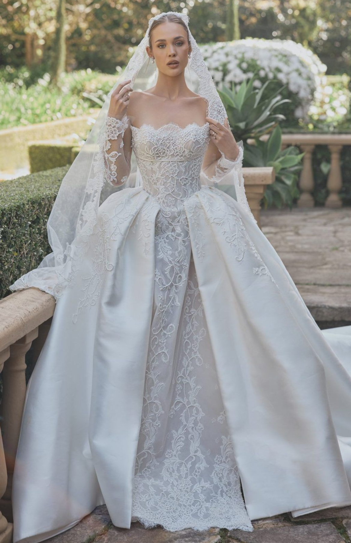 A woman is wearing a white lace wedding dress with long sleeves.