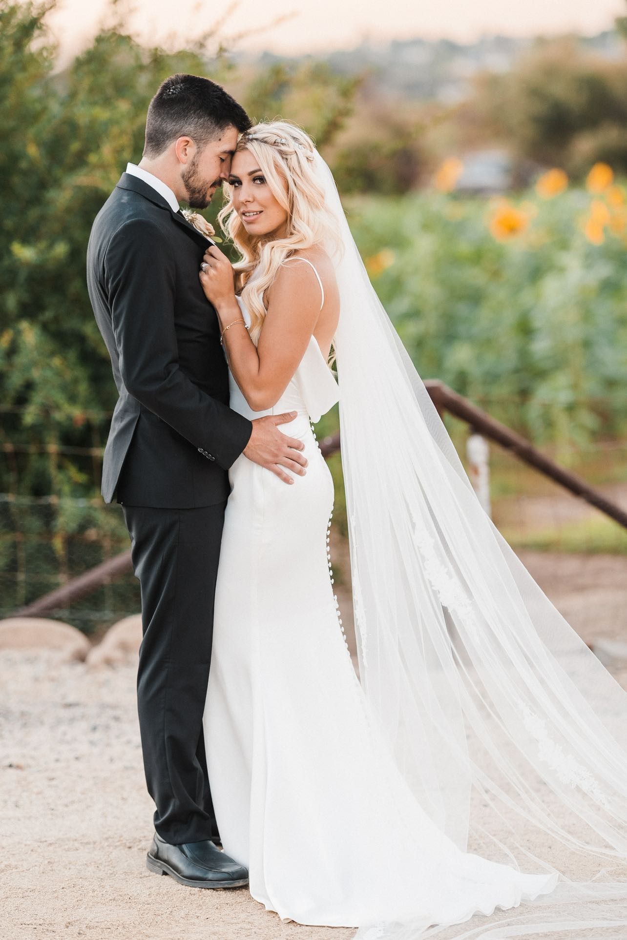 A bride and groom are posing for a picture in front of a field of sunflowers.