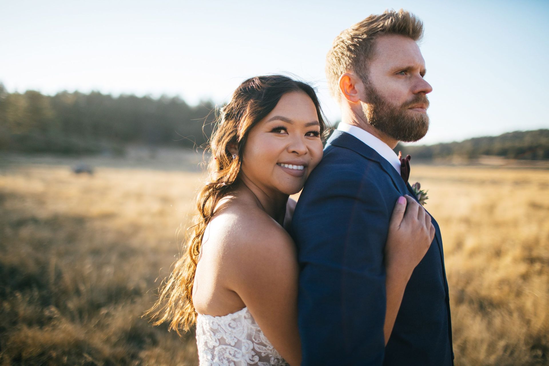 A bride and groom are posing for a picture in a field.