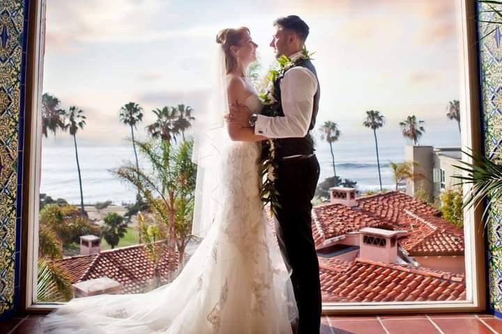 A bride and groom are standing in front of a window looking at each other.