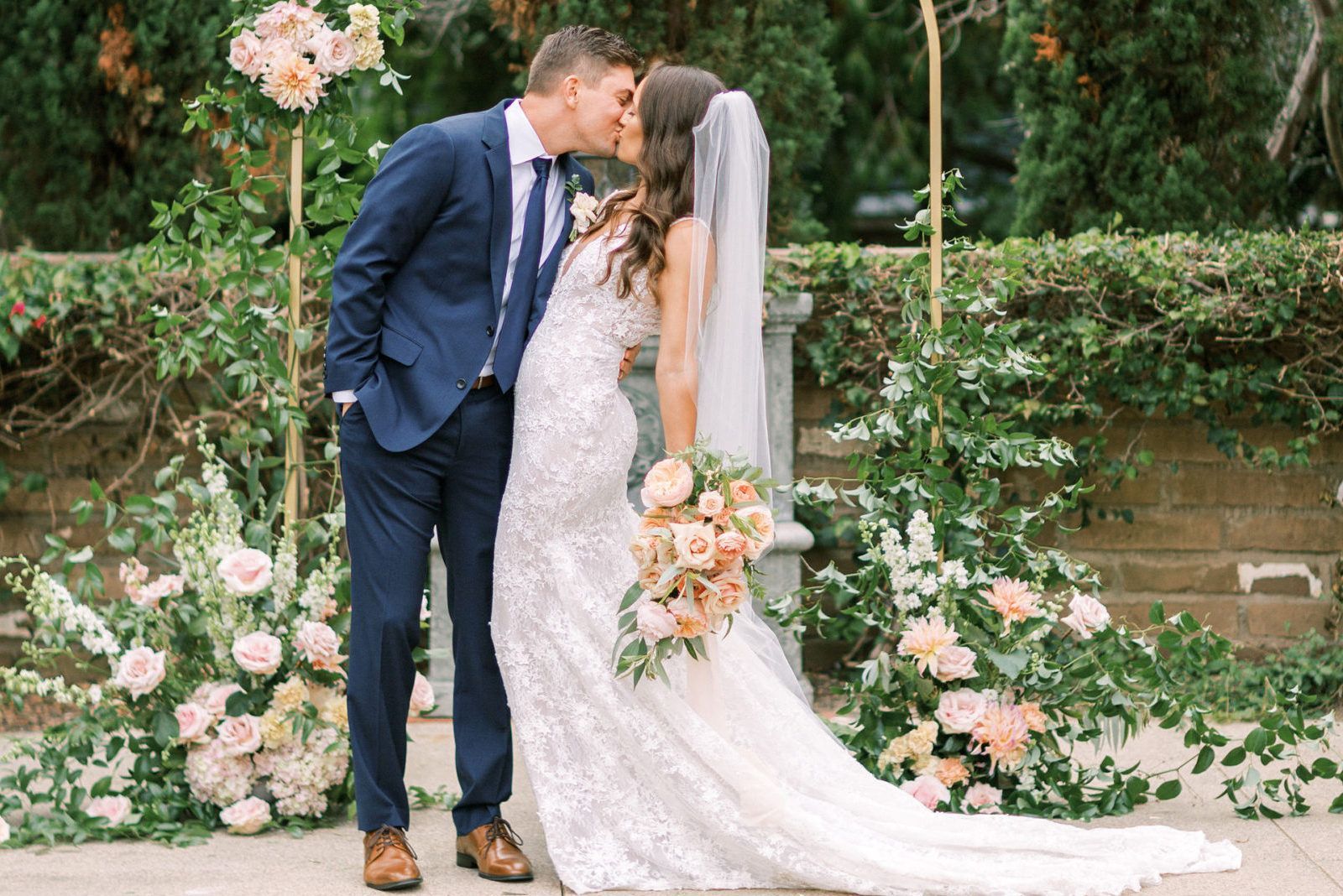 A bride and groom kissing in front of a floral arch.