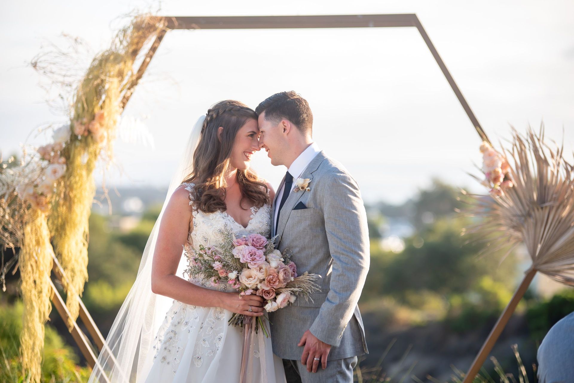 A bride and groom are standing next to each other in front of a wooden arch.