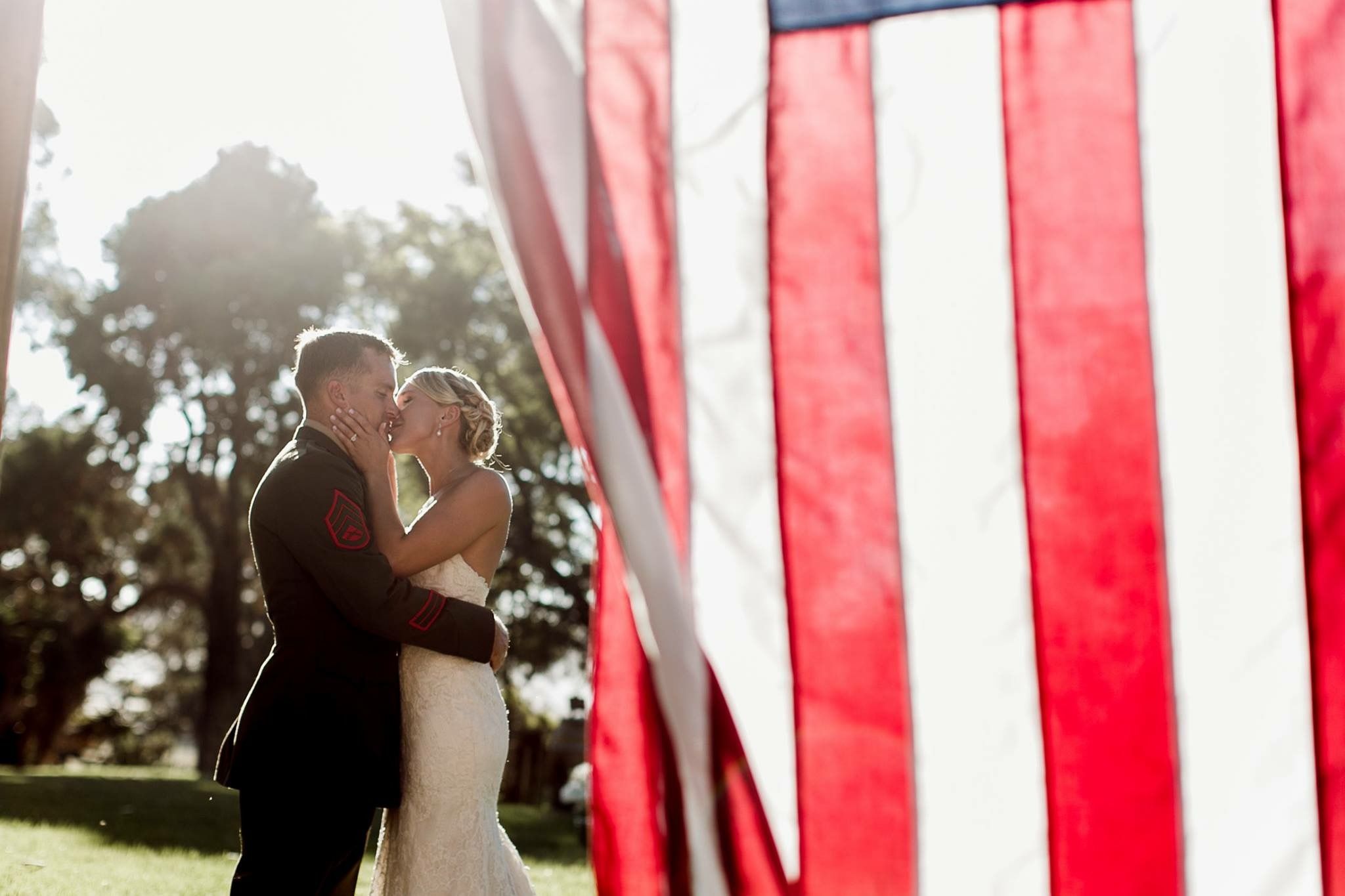 A bride and groom are kissing in front of an american flag.