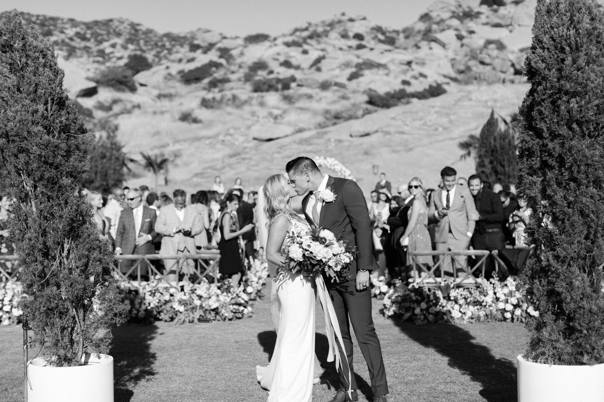 A black and white photo of a bride and groom kissing at their wedding ceremony.