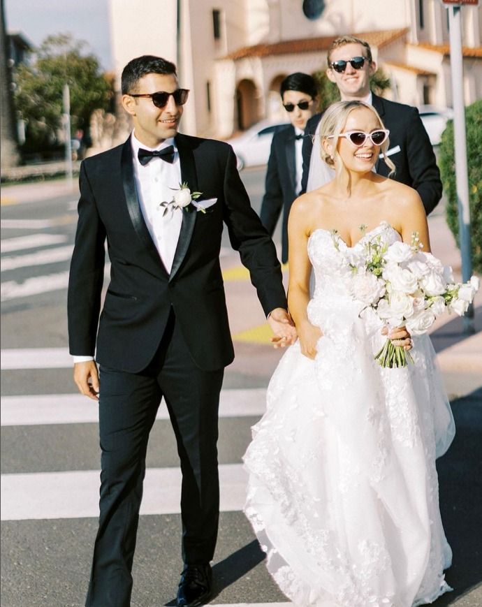 A bride and groom are crossing a street while holding hands.