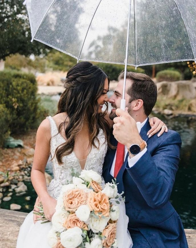 A bride and groom are kissing under an umbrella.