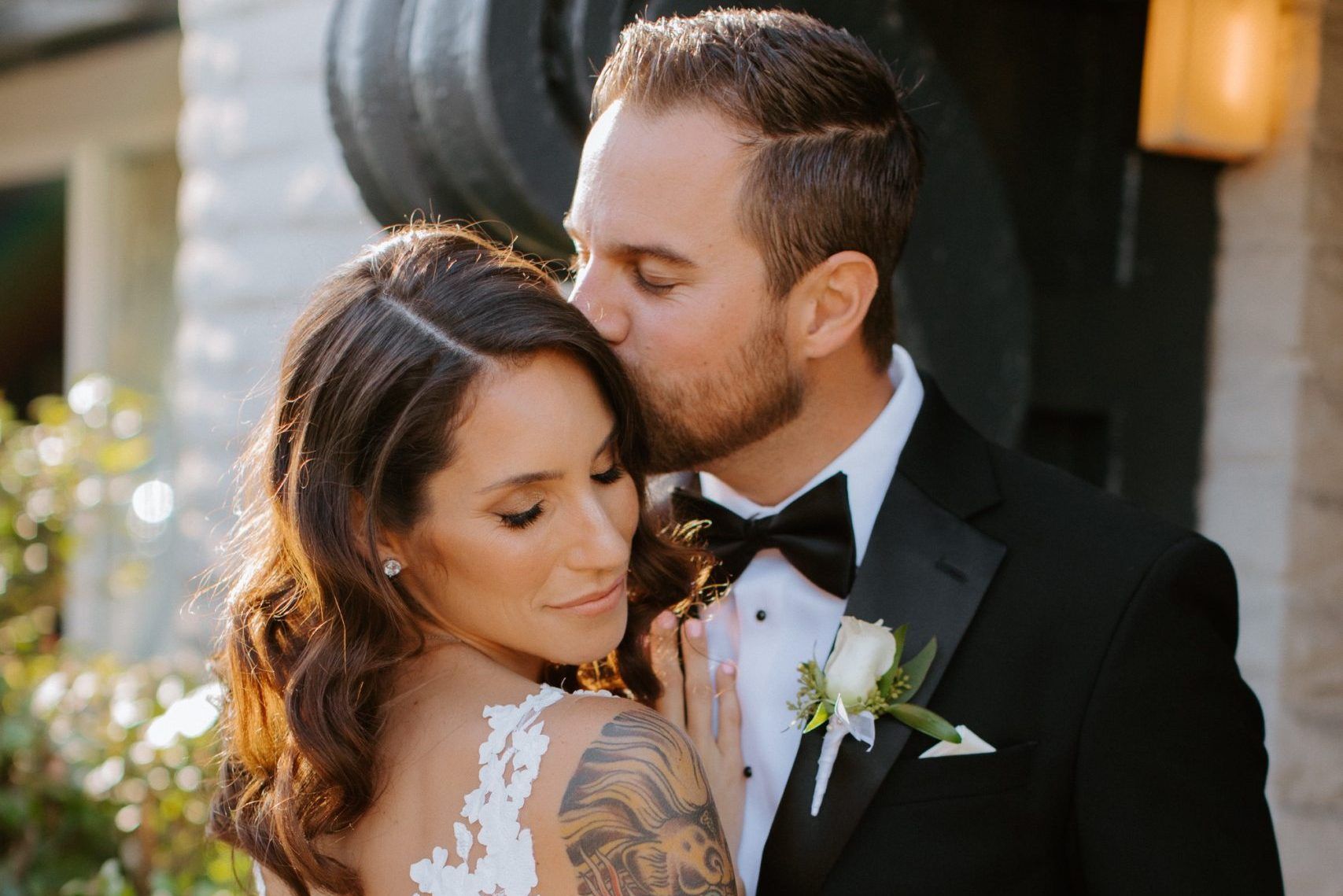 A bride and groom are posing for a picture and the groom is kissing the bride on the cheek.