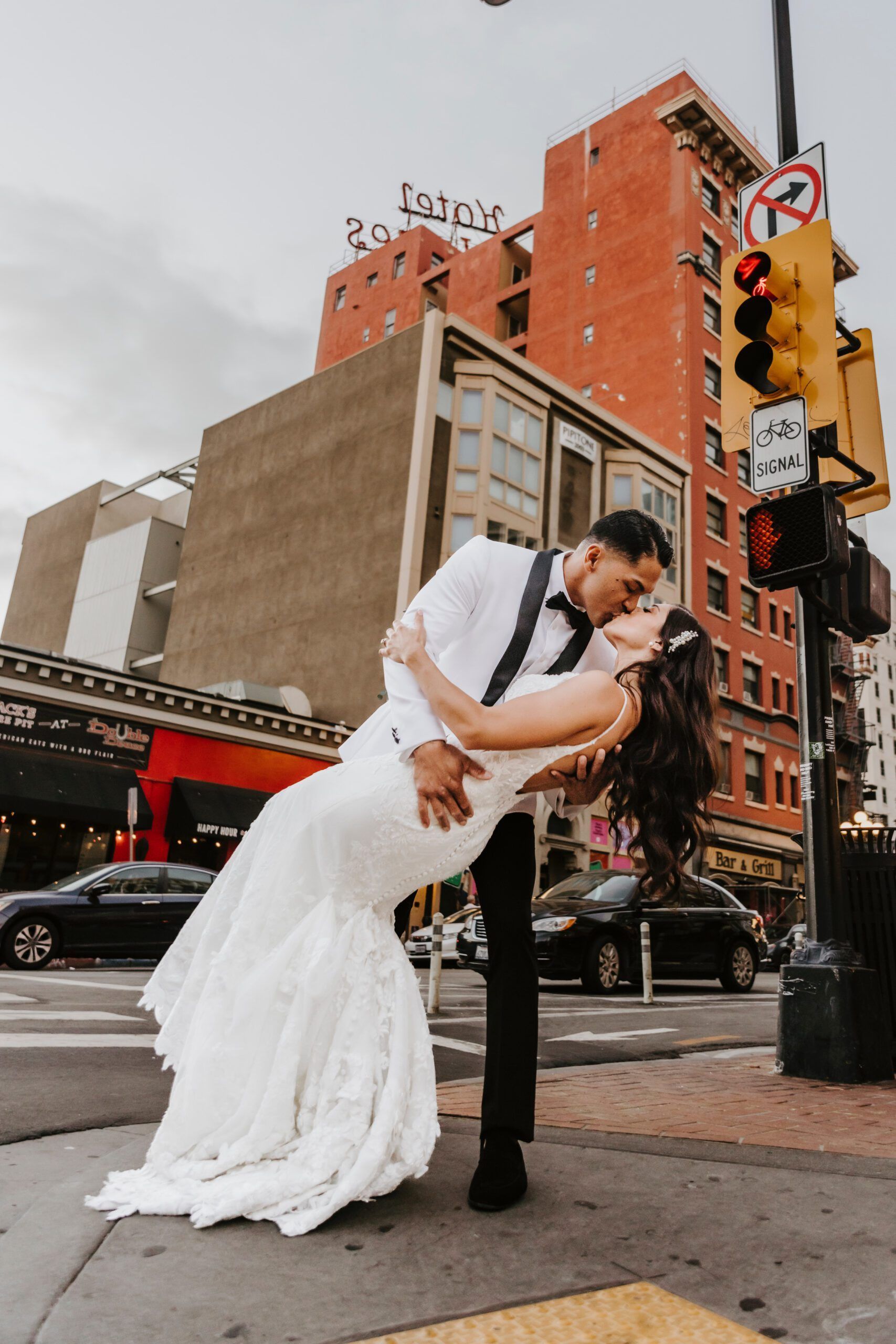 A bride and groom are kissing on the street in front of a building.