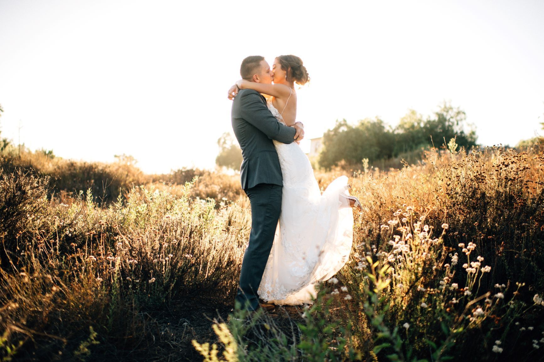 A bride and groom are kissing in a field of tall grass.