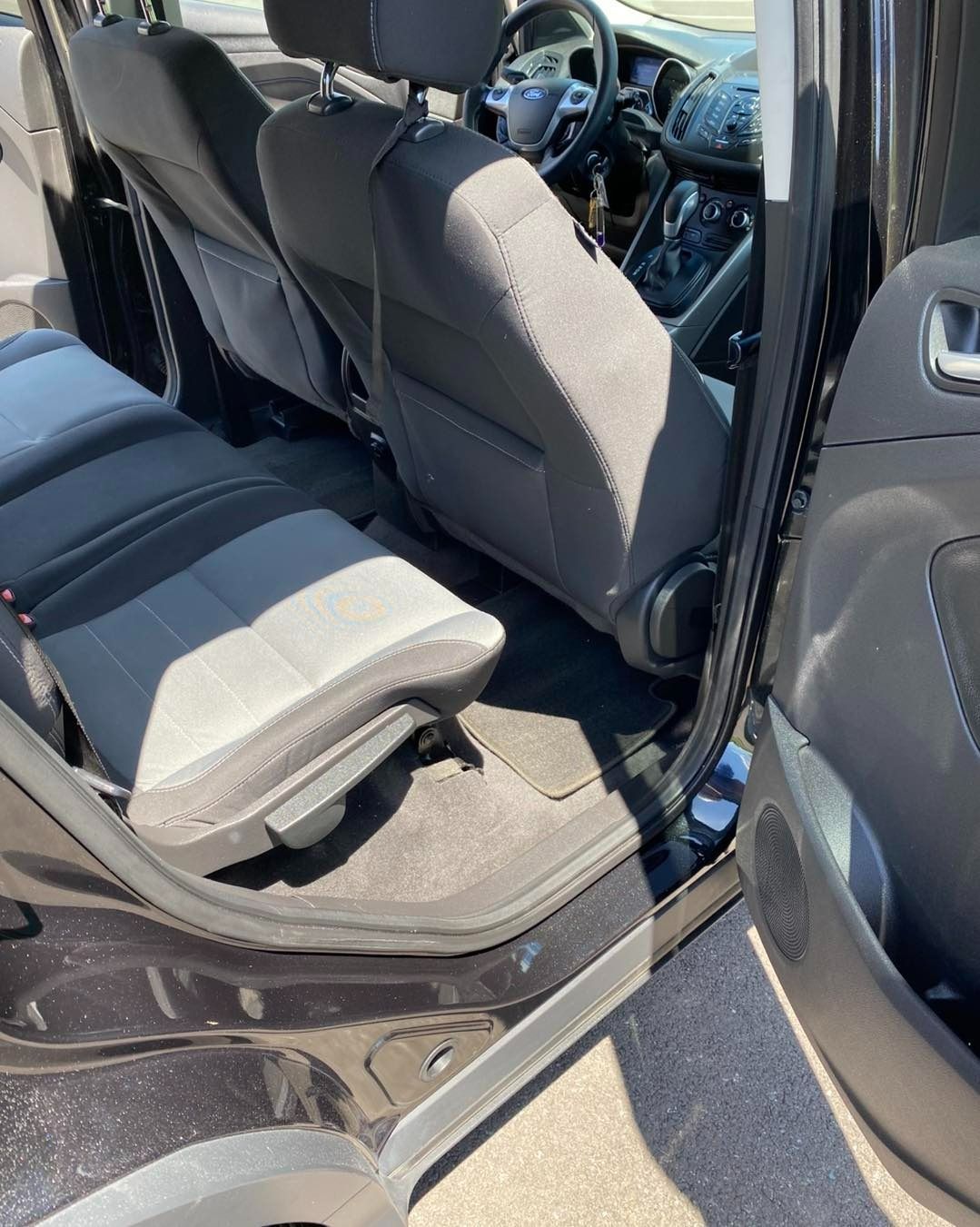 Inside of a black SUV: folded-up gray backseat, open door, black interior, floor mats, and front seats.