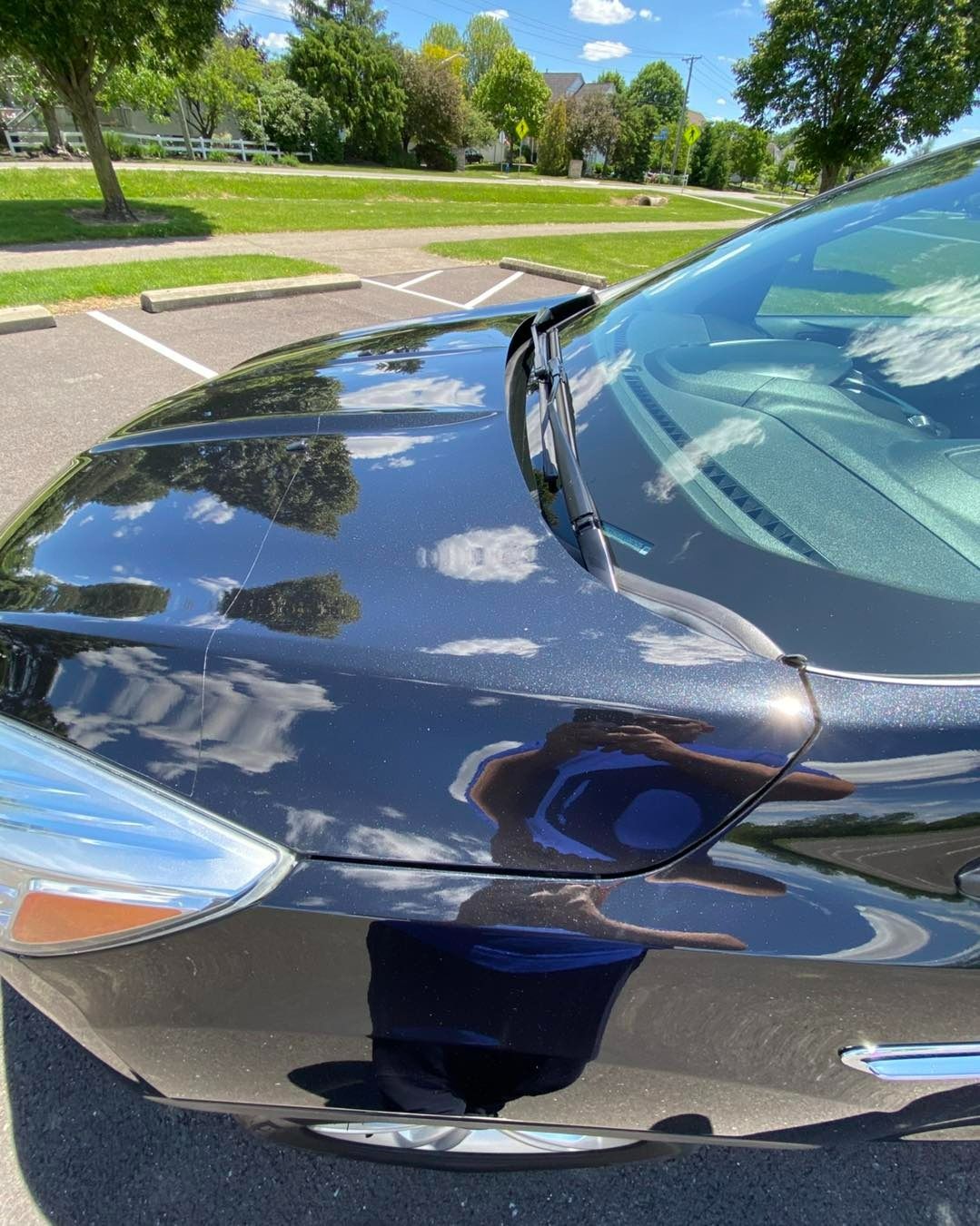 Black car hood reflecting sky and surroundings in parking lot.