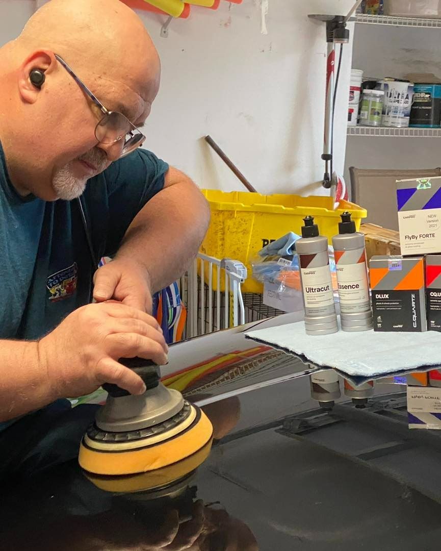 Man polishing a car hood with an electric buffer in a garage.