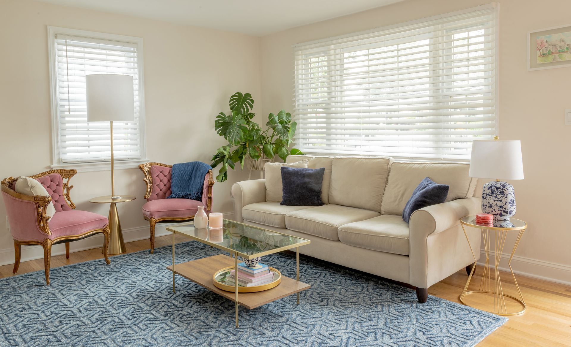 A bright living room with a beige sofa, two pink velvet chairs, and a blue patterned rug