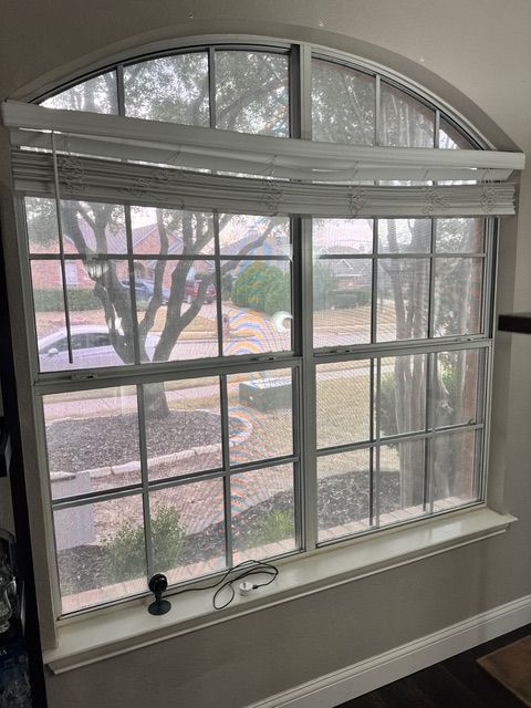 A large arched window with a broken, sagging set of white horizontal blinds, viewed from inside a room.