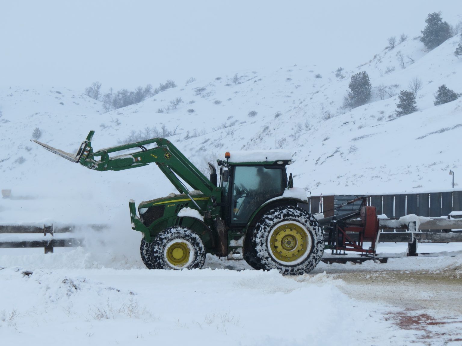 A john deere tractor is driving through the snow