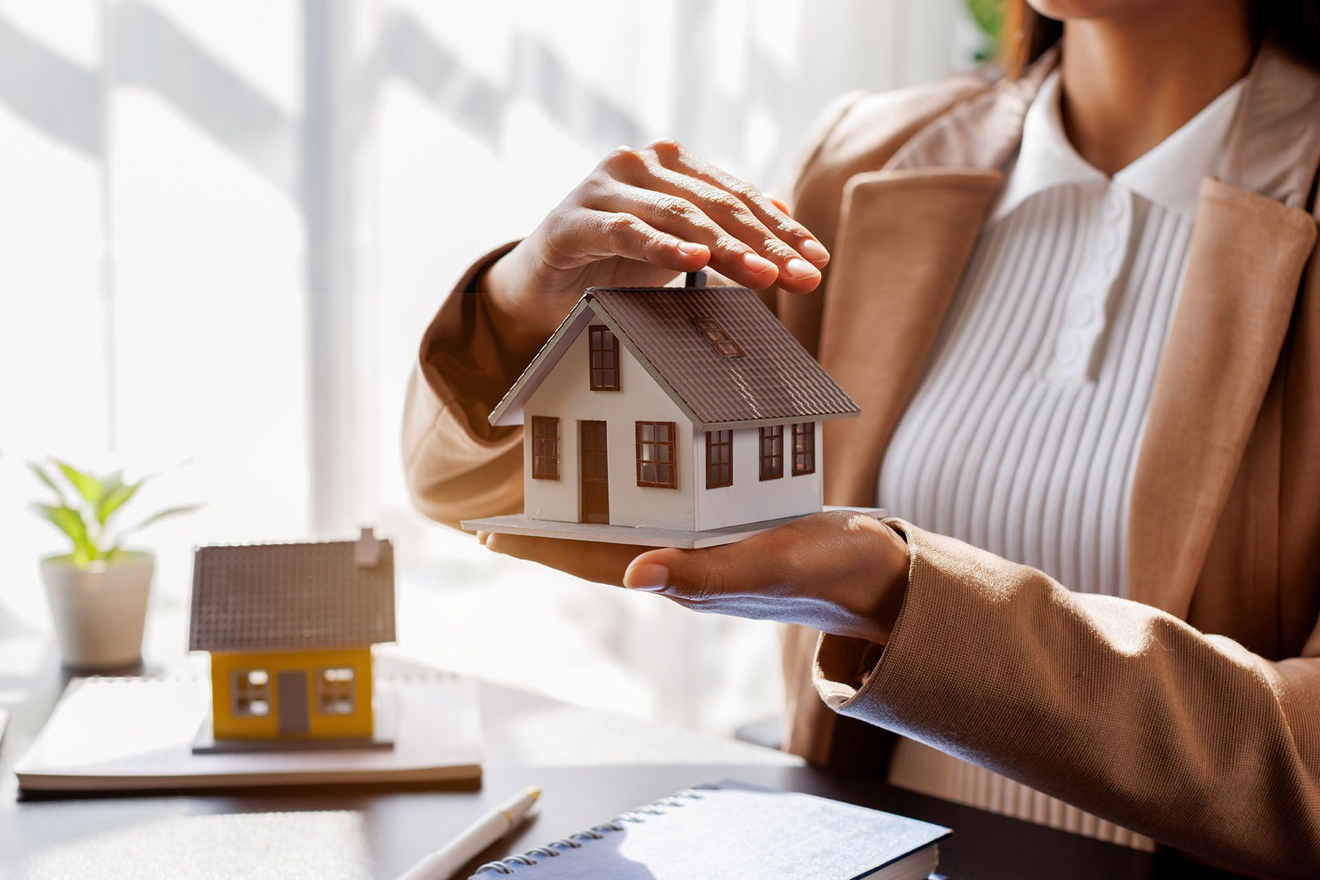 An expert from a home insurance agency holding a model house, symbolizing secure coverage.