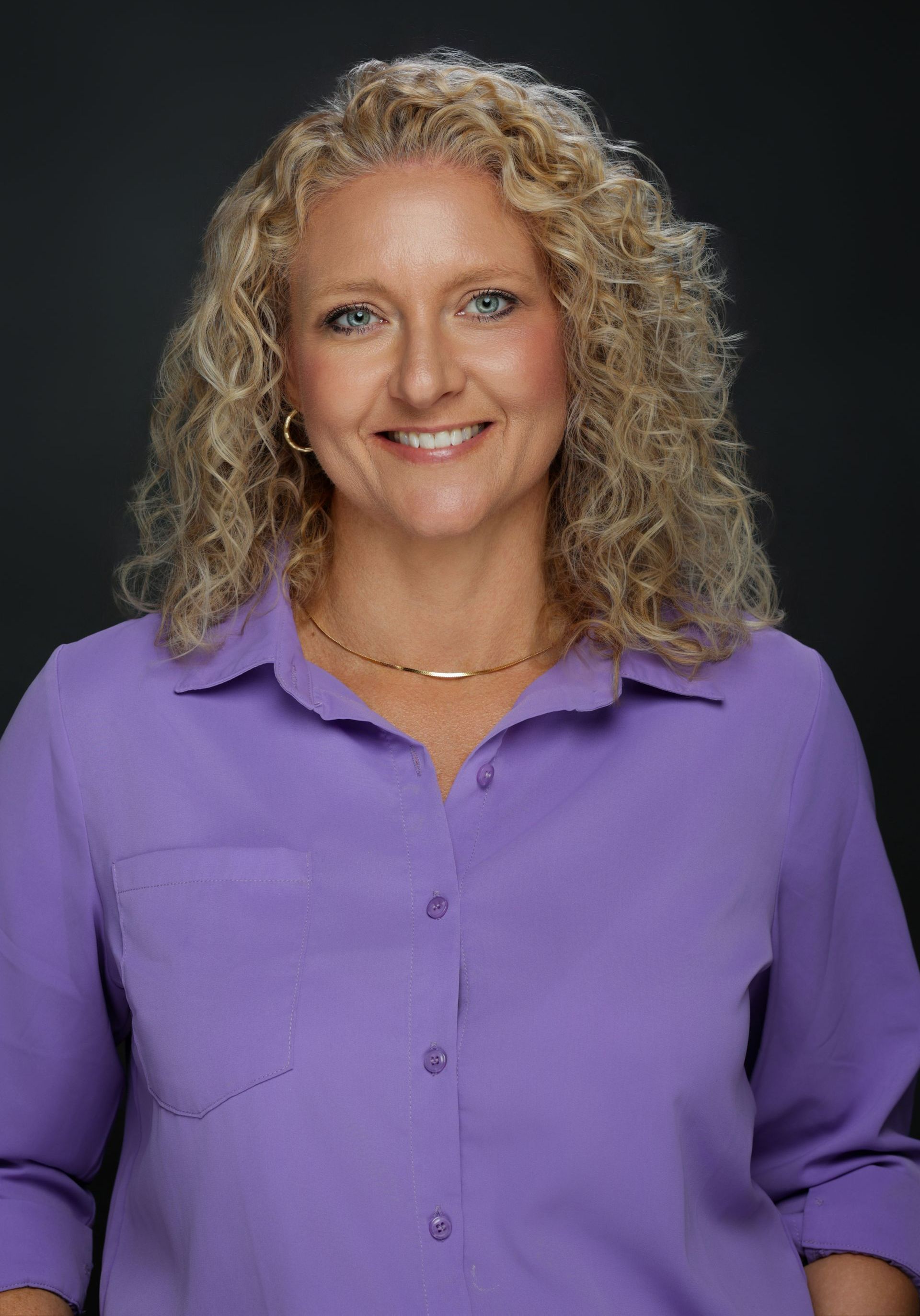 A woman with curly hair is standing in front of a sign that says ts.