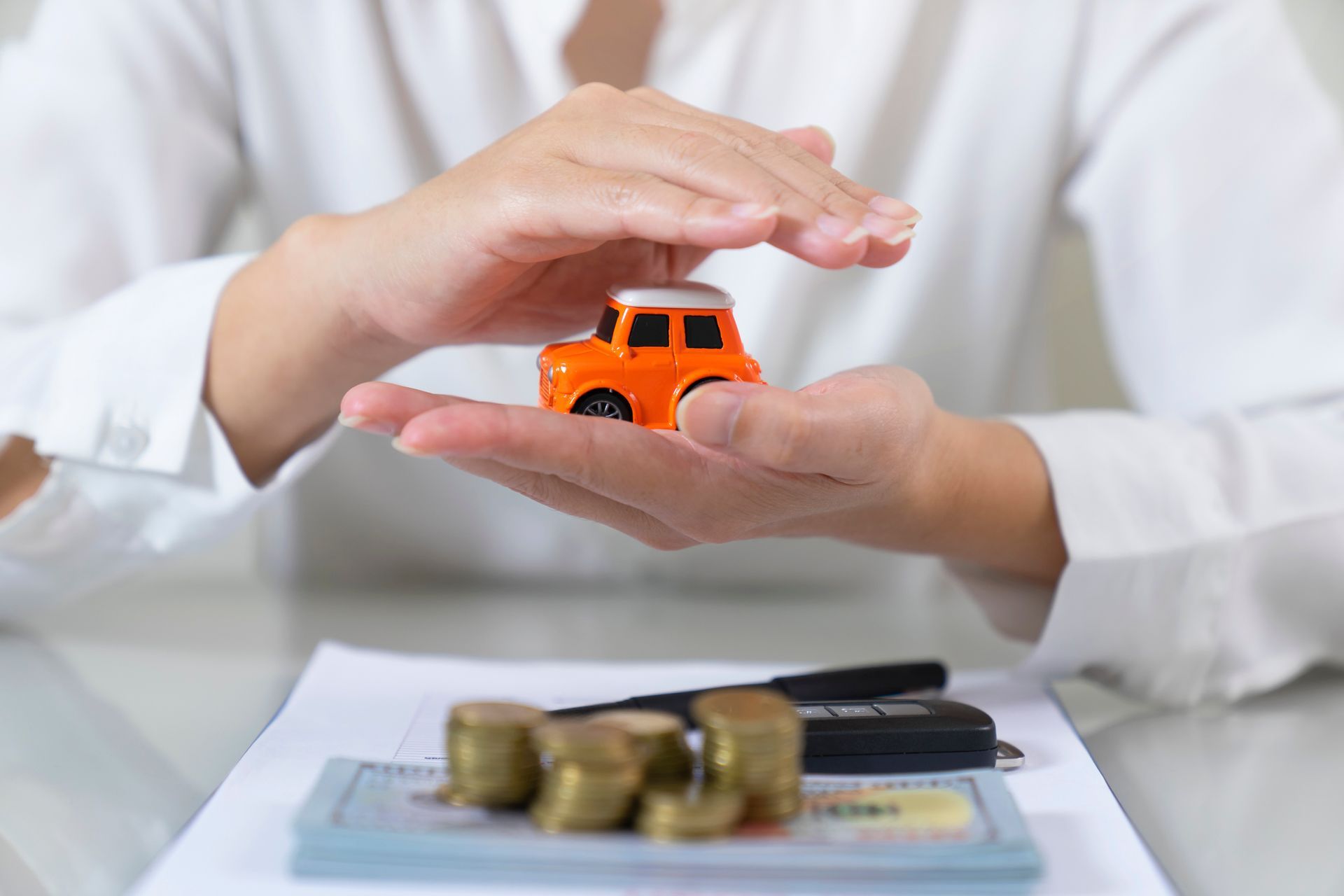 Hands Shielding Toy Car with Coins and Paperwork on Table.